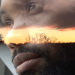 man looking out of a car with the sunset reflected on his face
