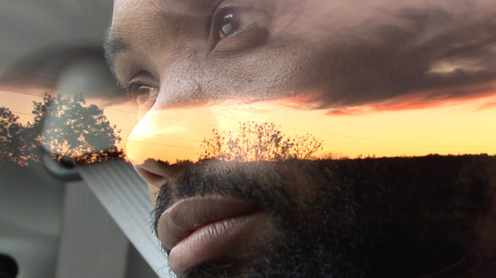 man looking out of a car with the sunset reflected on his face