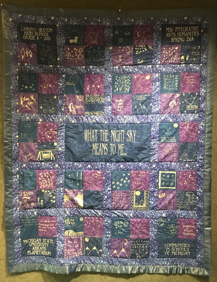blue and purple quilt that says "what the night sky means to me"