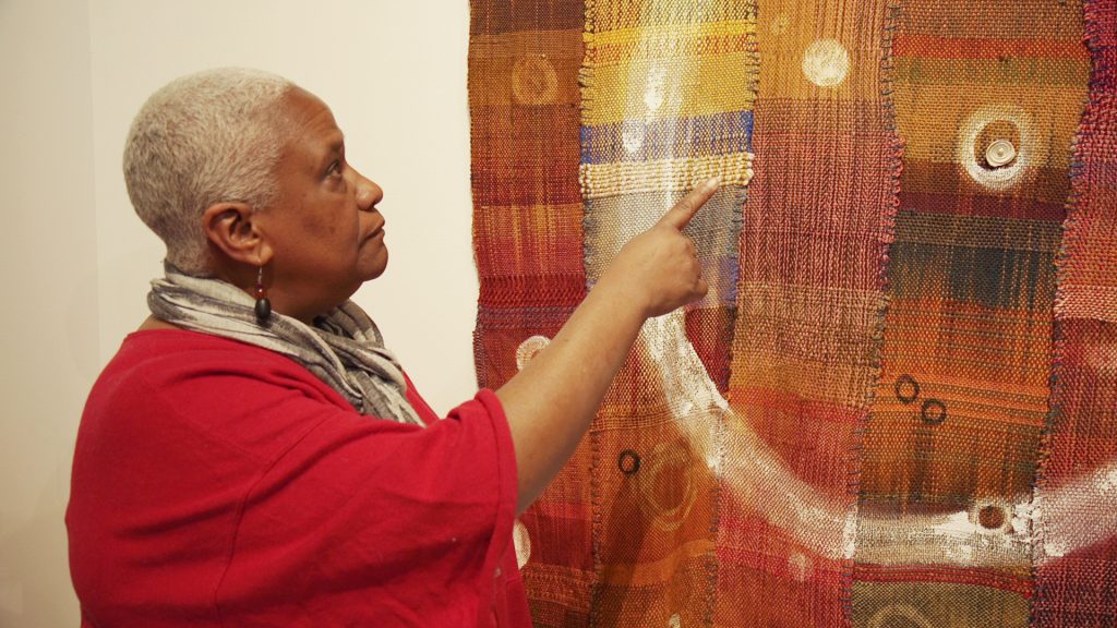 a women in a red shirt and white scarf showing her artwork