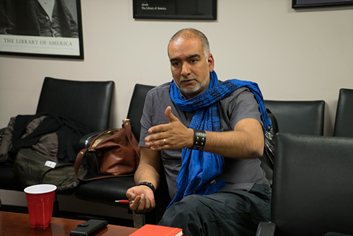 a man with facial hair wearing a grey shirt and blue scarf talking