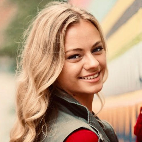 girl in a collared vest and blonde hair looking back at the camera and smiling