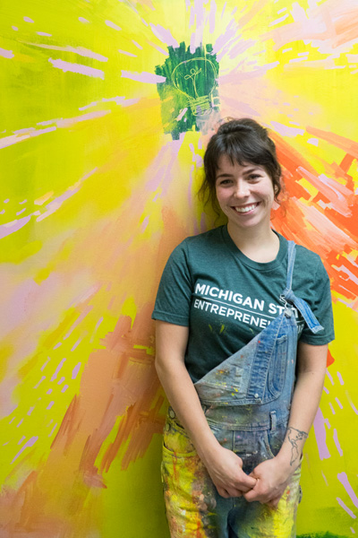 A girl in overalls standing in front of a mural