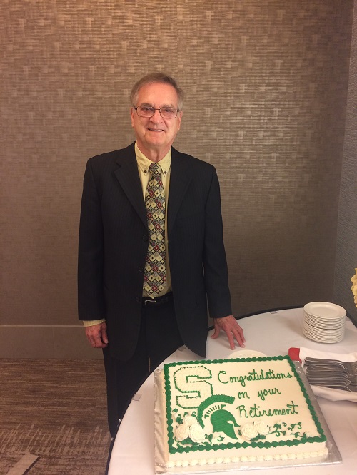 a man in a suit with glasses standing next to a cake 