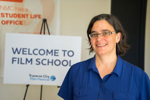 woman in glasses in front of a sign that says "welcome to film school"