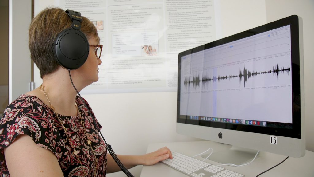 Woman wearing black headphones is looking at a computer 