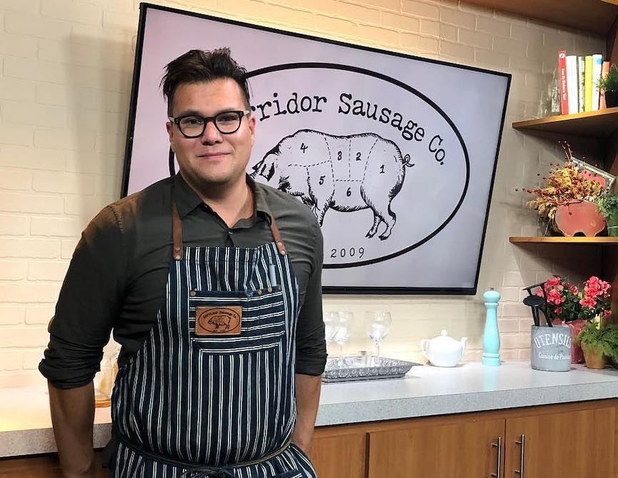 man who is wearing a striped apron and smiling softly while standing in front of a counter that has glasses and books on it