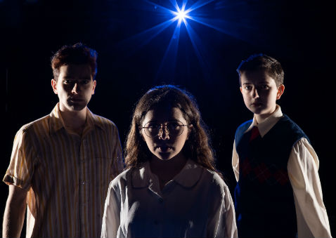 Two boys and a girl standing in the dark with a blue light shining on them