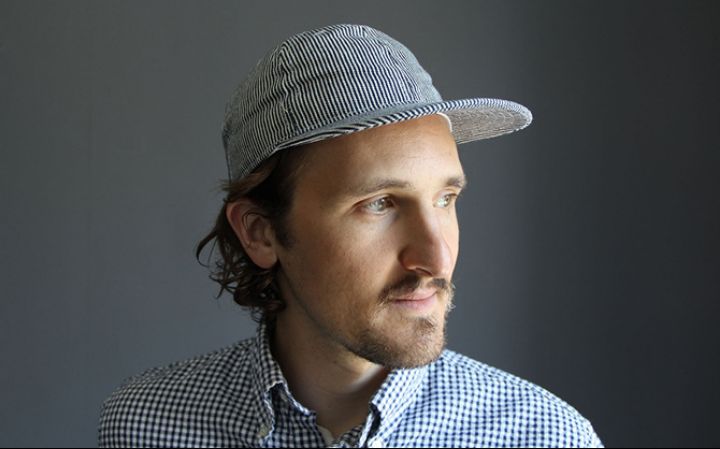 a man with facial hair wearing a hat and a blue checkered button down shirt