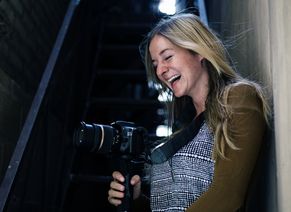 a woman with blonde hair wearing a black and white shirt and brown cardigan holding a camera