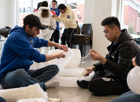 two men sitting on the ground who are holding giant white plastic wrap and strings