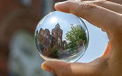 hand holding a glass ball that is reflecting an orange brick building with a bell tower