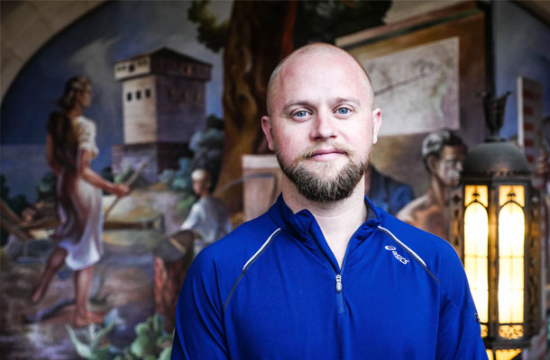 man wearing a blue zip-up who has slight facial hair and is looking at the camera and is standing in front of a mural