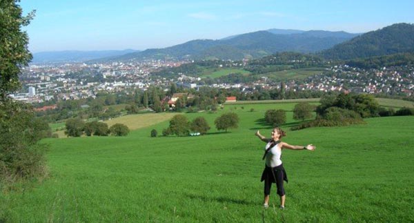 image of girl with arms outstretched in a field, buildings and mountains in the distance