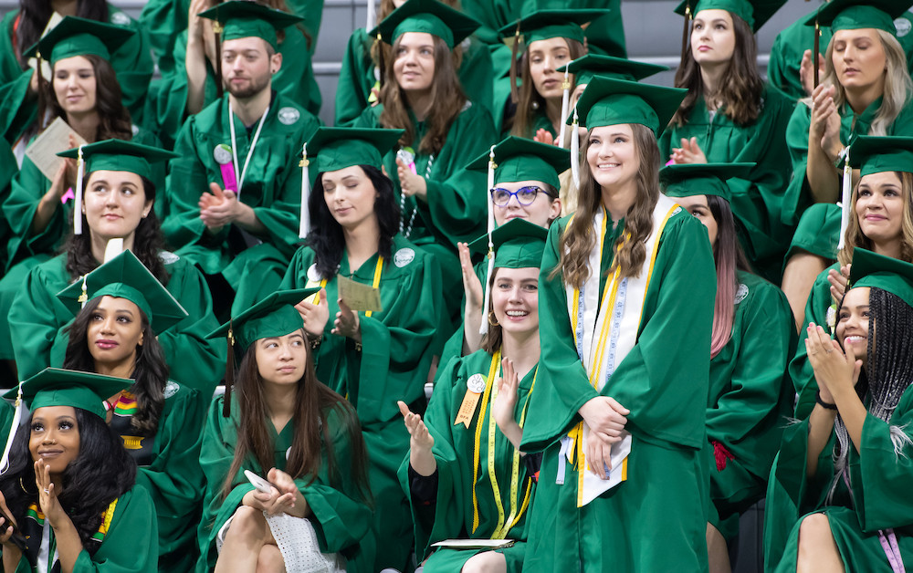 group of young people all wearing green graduation robes and caps who are smiling and clapping