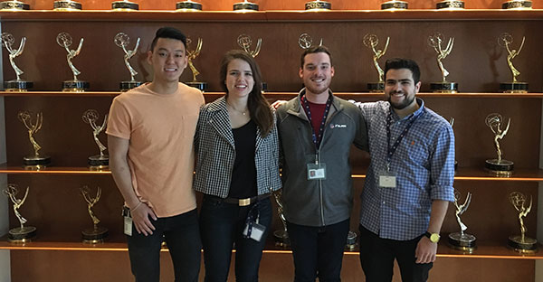 four interns standing in front of several shelves filled with Golden Globe awards