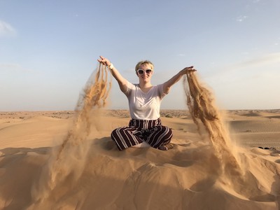 a girl in a white shirt and red pants sitting in the sand