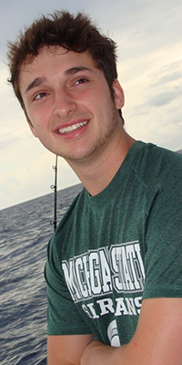 portrait of a man with dark hair and wearing a t-shirt that says 'Michigan State Spartans'