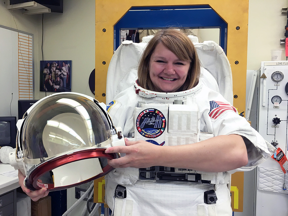 A smiling woman wearing an astronaut suit.