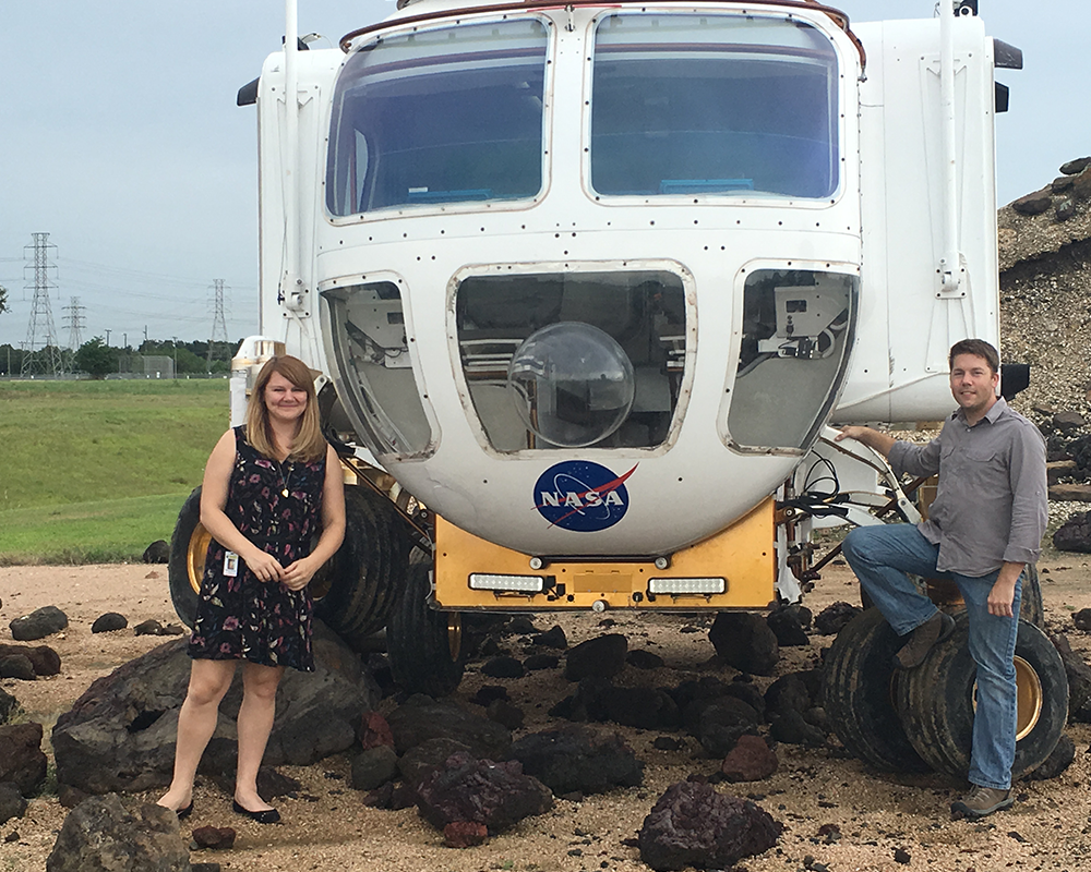 A woman and a man standing in front of a NASA space rover vehicle.
