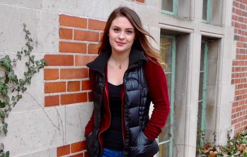 a girl with long brown hair wearing a red long sleeve jacket with a black vest and black shirt underneath
