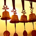 A row of bells hanging from ribbon in front of the setting sun
