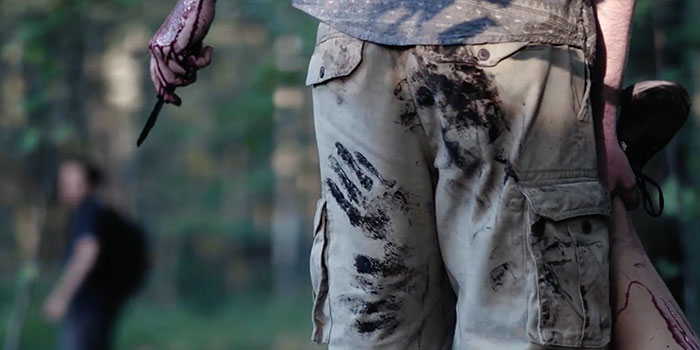 picture of the back of a man's pants with blood splatters, the man is holding a bloodied knife