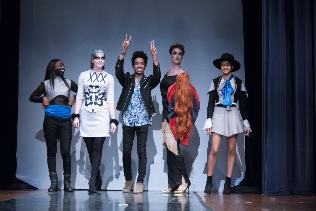 man posing on stage with models in his designs