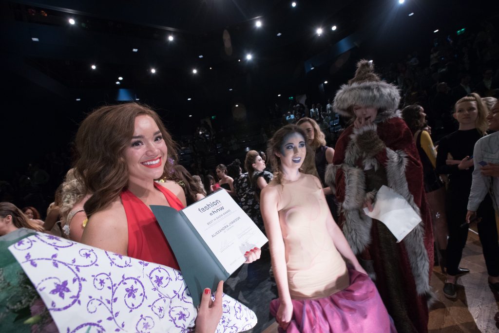 woman with brown hair in red dress posing with her award next to models
