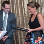 woman in dress receiving award from man with glasses