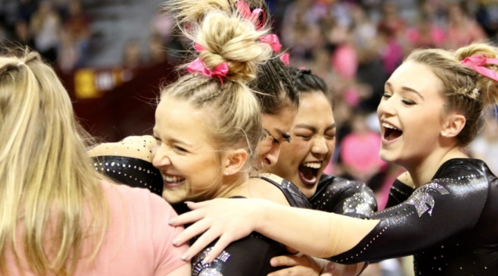four girls hugging with pink bows in their hair wearing black leotards 