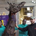 metalwork giraffe standing in the middle of three people smiling