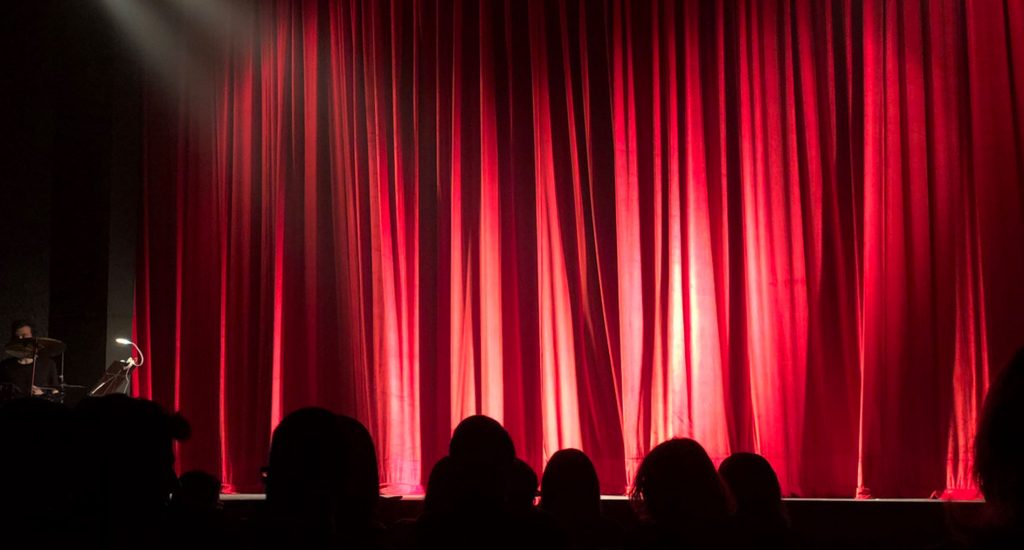 red curtain on a stage, closed, with shadowed audience