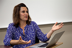 woman with brown hair sitting in front of laptop talking to class