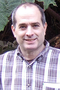 close up of balding man wearing a plaid button up shirt smiling