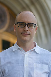 close up of man with no hair and glasses wearing a white dress shirt
