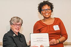 two woman both wearing glasses, one giving the other an award
