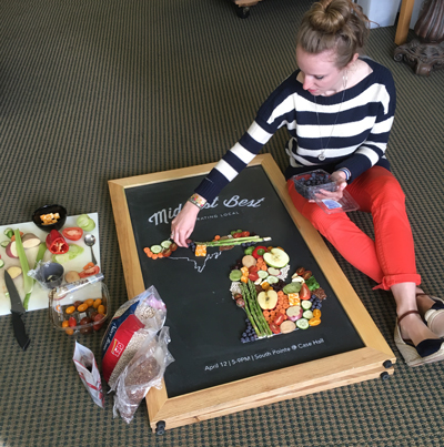 woman working on local food poster, putting together fresh food in the shape of michigan
