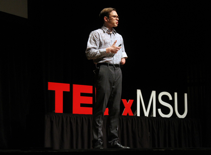man speaking on stage at TEDxMSU
