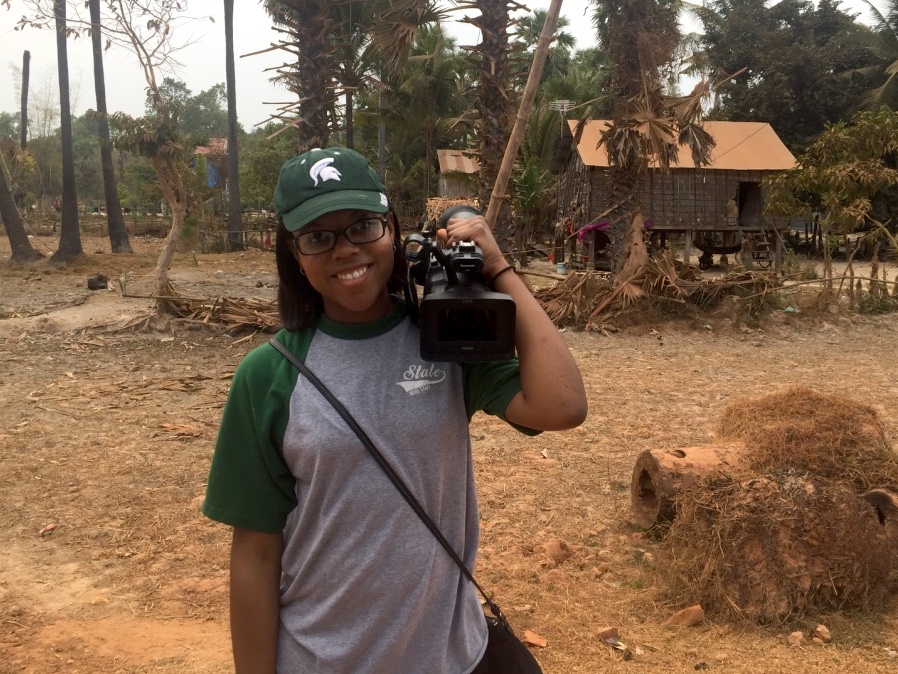 woman who's wearing a Michigan State shirt and hat and holding a camera on her shoulder 