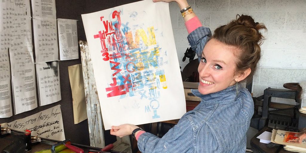 Kelly smiling and holding up a letterpress print