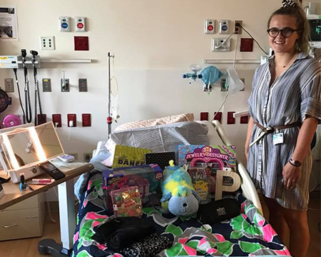 woman in dress with glasses posing with hospital bed that she decorated