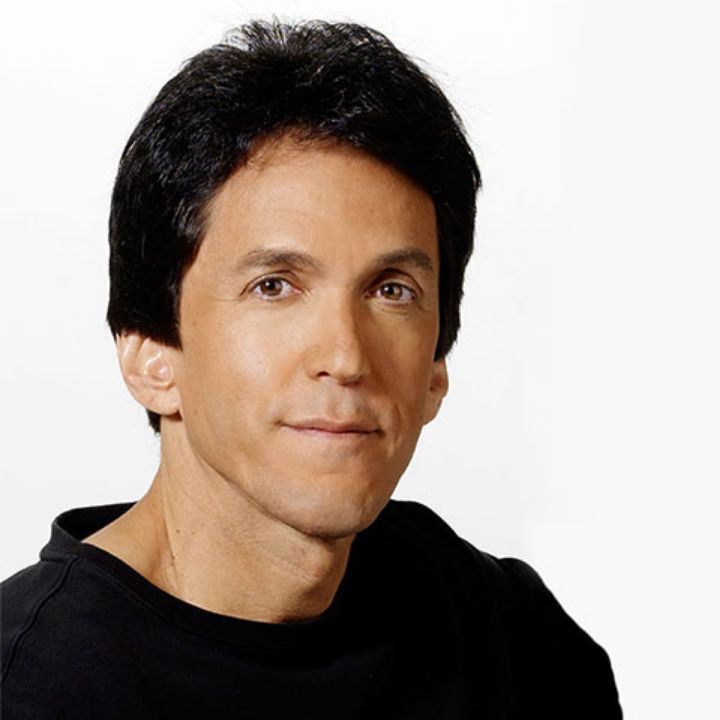 Man with dark brown hair in front of white background wearing a black shirt 
