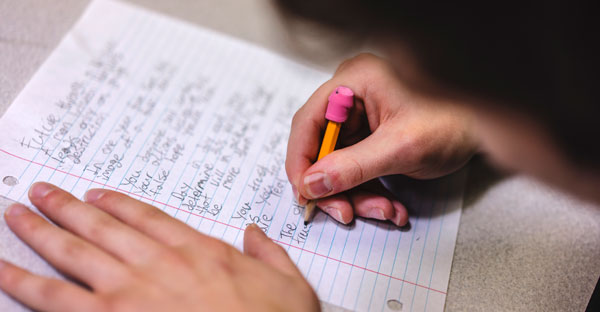 closeup of a student writing on lined paper with pencil