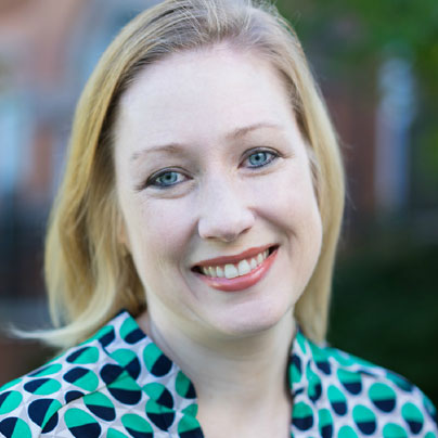 headshot of a blonde woman wearing a patterned shirt that is green, black, and white