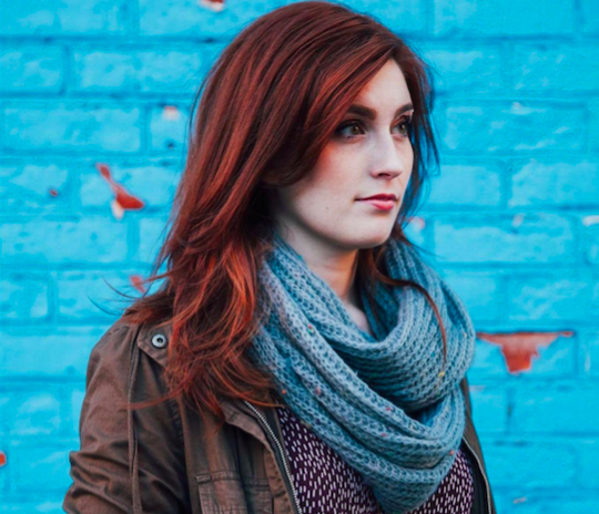 portrait of a woman with red hair in front of blue brick wall