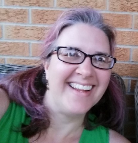picture of a woman smiling, she has shoulder-length hair, rectangular glasses, and is wearing a green tank top