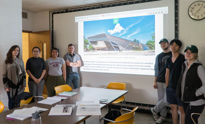 7 students pose in front of projected screen in classroom