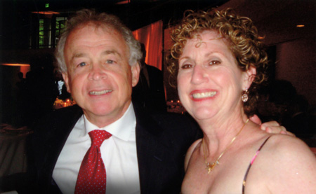 a man in a black suit with a white button down shirt and red tie and a lady with curly short hair in a dress