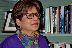 Woman with short dark hair and glasses standing next to a bookcase